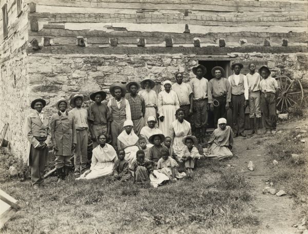 A production still for the Fox Hearst film "Romance of the Reaper." The film was produced by International Harvester at Walnut Grove to celebrate the Reaper Centennial. A group of African-Americans, probably local residents, are posing near the McCormick blacksmith shop. Some or all of them may have appeared as extras in the film.