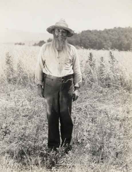A production still for the Fox Hearst film "Romance of the Reaper". The film was produced by International Harvester at Walnut Grove to celebrate the Reaper Centennial. A man with a long beard and dressed as a farmer is posing for a photograph in a field. The man may have been a local resident recruited for the film.
