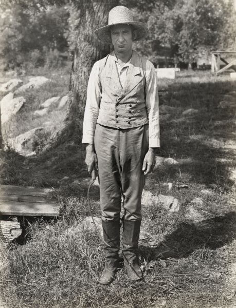 A production still for the Fox Hearst film "Romance of the Reaper". The film was produced by International Harvester at Walnut Grove to celebrate the Reaper Centennial. A man dressed as a farmer is holding a reaping hook in his right hand. The man may have been a local resident recruited for the film.