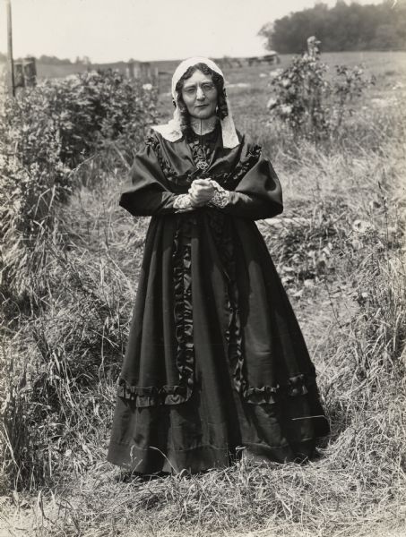 A production still for the Fox Hearst film "Romance of the Reaper". The film was produced by International Harvester at Walnut Grove to celebrate the Reaper Centennial. Actress Geraldine Woods stands in a field with her hands clasped in front of her.