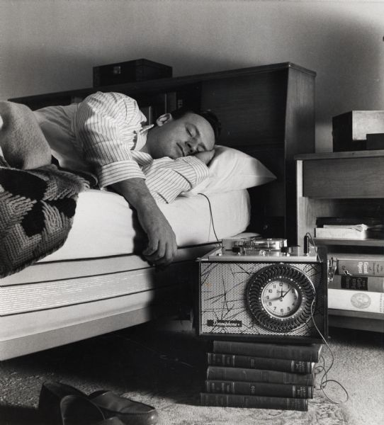 International Harvester truck dealer Vern Netteschiem listening to recorded truck specifications while he sleeps. The Dormiphone was a clock-controlled tape recorder. According to a magazine article that accompanied the photograph, a "sales promotion man . . . taped a spec-studded sales pitch for the International Travelall, set it to replay softly (at 2:00 and 4:00 a.m.), through an under-pillow mike, into the ear of IH Dealer Vern Netteschiem, while he slept . . . After a peaceful night's sleep, Netteschiem found he could recall nearly 80 percent of the five-minute recording."