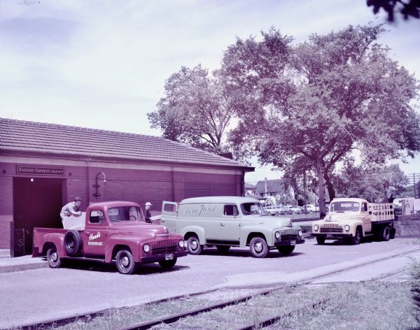 Color photograph of International L-120, L-110, and L-130 trucks outside of a long building.