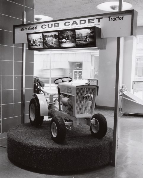 A Cub Cadet lawn tractor is on display in a showroom, possibly at the International Harvester headquarters building in Chicago, Illinois. The tractor is described as: "compact...versatile...job-matched equipment for all lawn and garden chores."