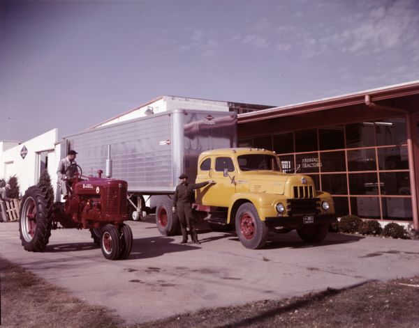 View of an International R-205 Sleeper Cab Truck with closed top van semi-trailer outside a Farmall dealership. The truck is parked next to a man operating a Farmall Super M tractor.