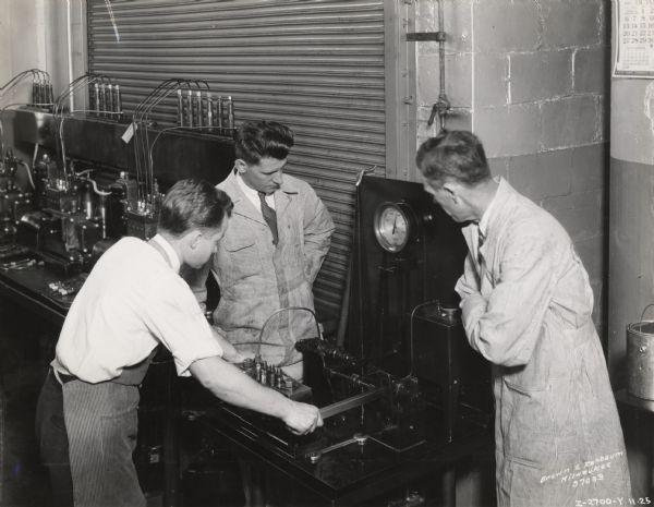 Original caption reads: "Milwaukee Works [factory] - Branch service managers watching tests of Diesel injection pump nozzles. Taken by McQuinn".