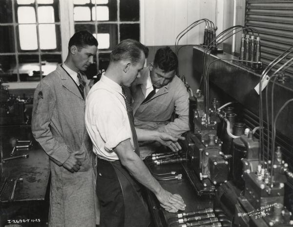 Branch service managers watch a test at a factory (most likely International Harvester's Milwaukee Works). Caption on photograph reads: "Branch service managers in injection pump testing room. Taken by McQuinn".
