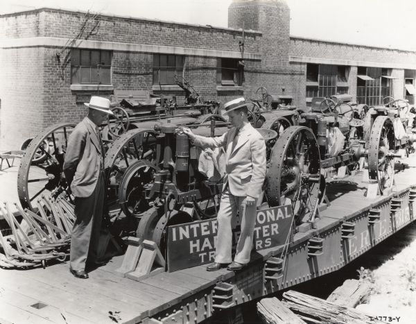 Two well-dressed men are standing outdoors among Farmall tractors which are loaded on railroad cars. Original caption reads: "M.E. Merseran, manager, and H.W. Martin, assistant manager, Boston general line branch."