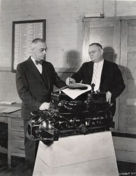 Two well-dressed men inspect an engine at the Farmall Works factory. Original caption reads: "Farmall Works, G.H. Jantg (left) chief inspector and S.A. Shappe, eng. dept."