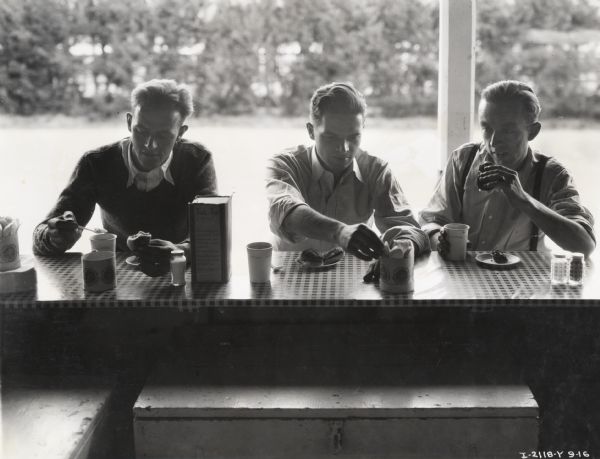 Truck drivers eat at an outdoor lunch counter. Original caption reads: "Elliott Taylor (center) and 2 truck drivers."