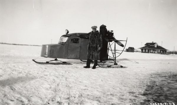 Edmonton branch house employee E. Swinton wearing a fur coat and standing next to a propellar-driven snowmobile. Original caption reads: "E. Swinton, Edmonton, Alberta, branch, International Harvester Company of Canada, Ltd., collects and sells by "Snow-mobile."