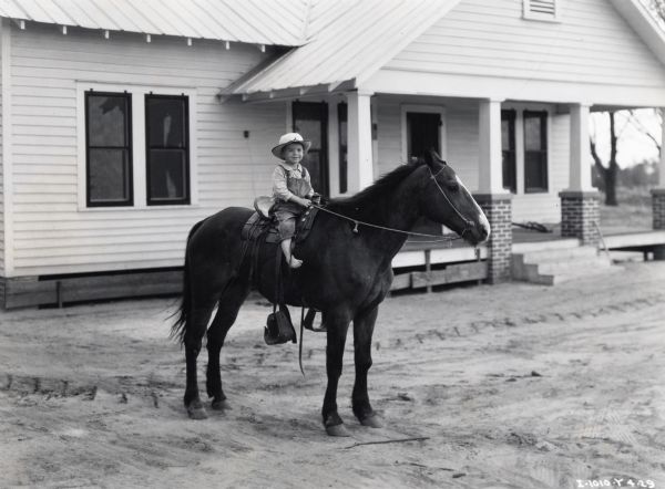 A young boy sits on a horse in front of a house. Original caption reads: "Son of E.D. Champion, Albany Georgia. We worked one whole day on Mr. Champion's farm making pictures of his F-12, and this picture of his son was a thank you job for him. [Taken by] Hyde and Hawkins."