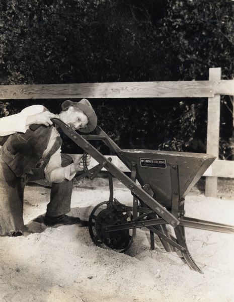 A man kneels to inspect and adjust a McCormick-Deering planter. The planter appears to be part of an indoor museum display.