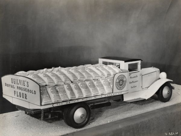 A miniature model of an International truck. The model carries cargo and reads: "Ogilvie's Royal Household Flour." Caption on photograph reads: "Miniature International made by Norman Scott, Winnipeg, Manitoba."