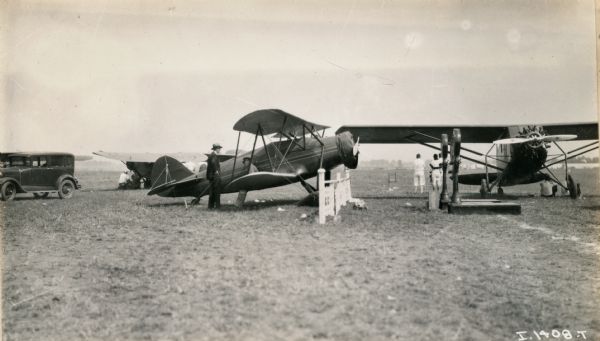 Three airplanes are parked in a field. Several men and a woman are standing and sitting among the airplanes. The event was likely the National Air Show in Chicago.