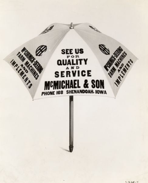 An umbrella with advertising for an International Harvester dealership. The text on the umbrella reads: "See us for quality and service/ McMichael & Son/ Phone 168 Shenandoah, Iowa".