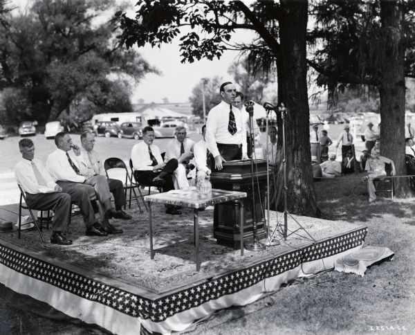 Earl C. Smith, president of the Illinois Agricultural Association, speaks into a microphone at an event to honor Mr. Clarence Dauberman for creating the first high compression tractor in the United States.