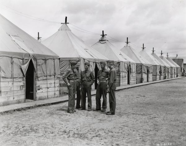 Five men stand and converse outside a row of tents at Fort Sill. Draftee Charles J. Richard is among the men. Richard was a former International Harvester employee of Oklahoma City. A complete story was published in the August, 1941 edition of <i>Harvester Works</i>.