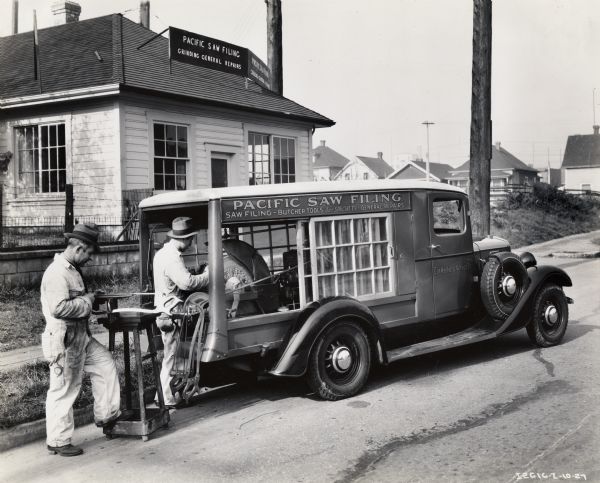 Two men sharpen knives with equipment carried by an International truck. Original caption reads: "C-5 equipped with special body, owned by John Ciffone, corner Keefer and Vernon Drive, Vancouver, British Columbia, who is engaged in meat knife sharpening and saw filing business. His helper shown at grindstone is William Richard."