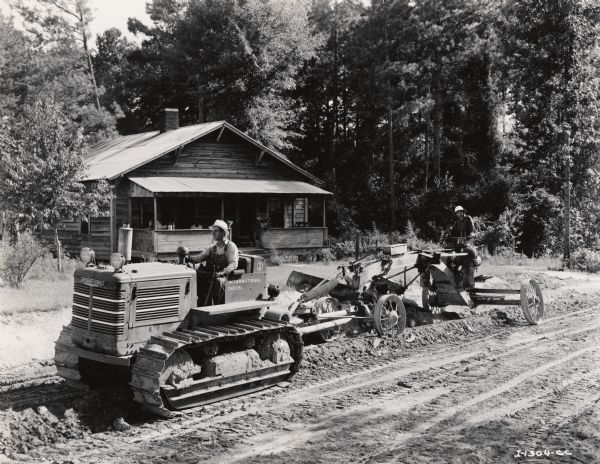 Men grade a new road surface with an International TD-14 crawler tractor (TracTracTor) and Adams Power Grader. There is a house in the background and people are sitting on the porch.
