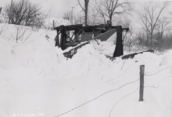 An International TD-14 crawler tractor (TracTracTor) with snowplow pushes through deep snow. Original caption reads: "Int. TD-14 Tractor equipped with front (?) 9-foot plow having 9 foot wings. Was owned by Henry Nichols of Fairfax, Vermont, who had a contract to clear about 90 miles of road in the towns of Fairfield and Swanton, Vermont. Taken by Albany Branch."