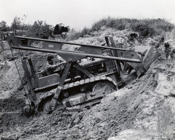 A man operates an International crawler tractor to dig an earthen pit. Original caption reads: "The city of Culver City makes use of the International TD-9 Diesel TracTracTor shown equipped with McCaffrey cable-operated 1 1/2-yard front-end loader to perform a variety of maintenance and construction work. It is shown at work in a borrow pit. The loader can easily be removed and a blade substituted for bulldozing."