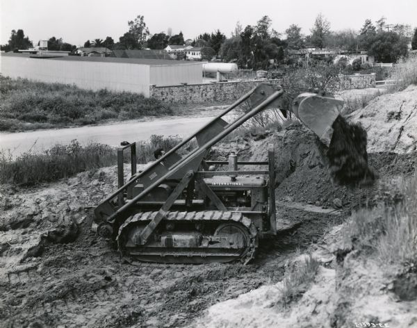 Man driving TD-9 TracTracTor (crawler tractor) digging in a pit. Caption on photograph reads: "The city of Culver City makes use of the International TD-9 Diesel TracTracTor shown equipped with McCaffrey cable-operated 1 1/2-yard front-end loader to perform a variety of maintenance and construction work. It is shown at work in a borrow pit. The loader can easily be removed and a blade substituted for bulldozing."