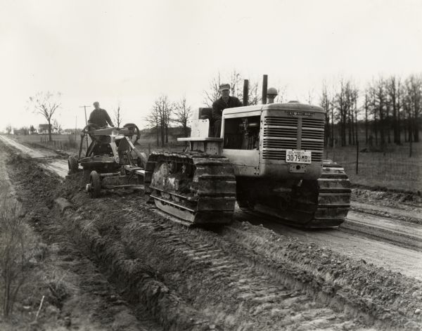 Men work on a new road with an International TD-18 TracTracTor (crawler tractor) and an Austin-Western grader. Original caption reads: "TD-18 T.T.T. and Austin-Western Grader owned by Van Buren County Paw Paw, Michigan grading county road four miles north of Kendall, Michigan. This work is done at the rate of 1.2 miles per day."