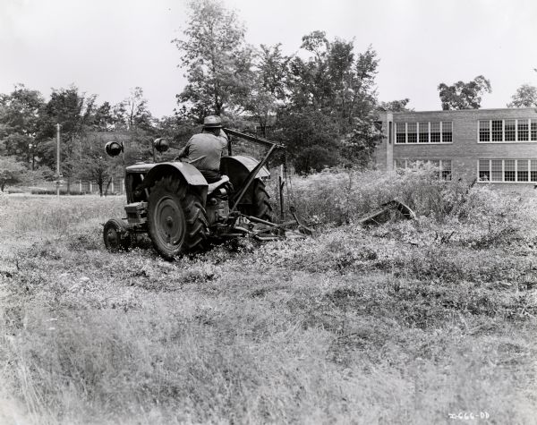 A man operates an International I-14 tractor with a six foot 112-V mower.