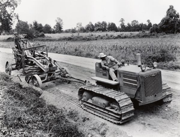 Elevated view of two men working with an International T-14 crawler tractor (TracTracTor) and an Adams grader to level a new road.