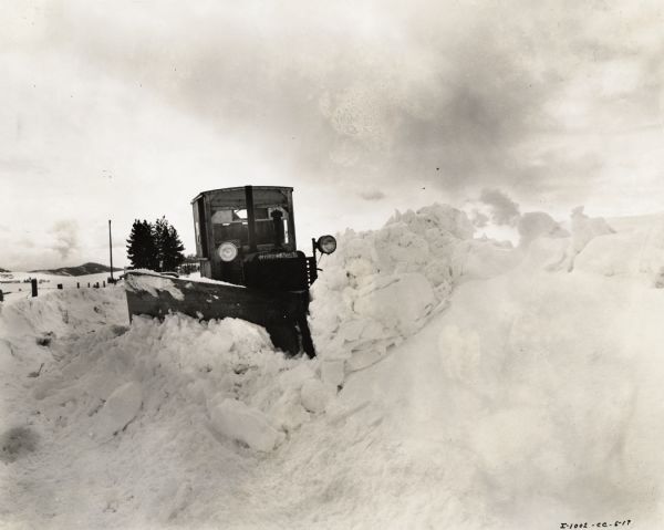 Man operating an International TD-35 crawler tractor (TracTracTor) and an Isaacson snowplow to clear a road in Kootenai County. According to the original caption, one to twenty miles were cleared per day, depending on the depth of the snow.