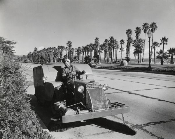 A man operating an International I-14 tractor and Hough street cleaner. The tractor was owned by the city of Santa Barbara. According to the original caption, the unit in the photograph swept twenty-six to thirty miles per day.