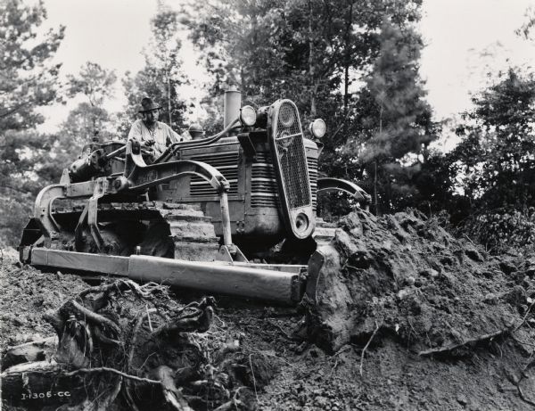 An International Harvester TD-14 crawler tractor (TracTracTor) with "B.E. Bullgrader" levels a mound of dirt for a highway exit. Original caption includes the note: "Taken by Hyde and Turner."