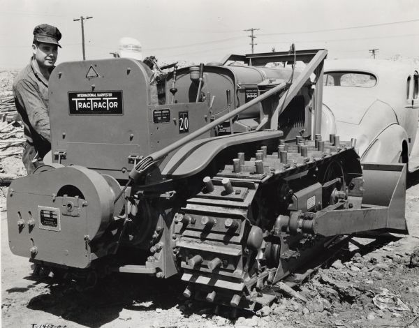 A man stands next to an International T-20 TracTracTor (crawler tractor). Original caption reads: "A T-20 TracTracTor (crawler tractor) and a McCaffrey bulldozer owned by R.W. Hampton Co. Los Angeles used on fill in of basement and foundation of May Co. new Wilshire store in Beverly Hills, California."