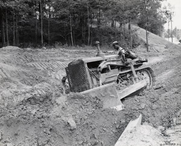 A man operates an International T-40 TracTracTor (crawler tractor). Original caption reads: "International T-40 TracTracTor equipped with bullgrader and used by the Pigford Brothers and Shuptrine Construction Company of Natchez on a 12-mile grading, drainage, and beautification contract on Section 3-W near the south end of the new Natchez Trace for 455 miles between Natchez, Mississippi, and Nashville, Tennessee."