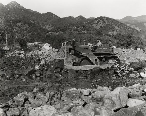 A man operates an International TD-18 TracTracTor (crawler tractor) to deepen a creek channel. Original caption reads: "TD-18 TracTracTor and Emseo(?) Bulldozer owned by C.W. Moore, contractor. This unit is deepening creek channel at Ojai, California."