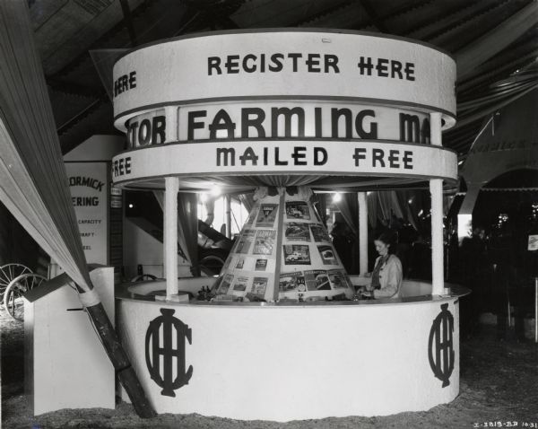 A woman stands in the International Harvester information booth at the Waterloo Dairy Cattle Congress in Iowa. There are advertisements for farm equipment and trucks. The booth bears the text: "register here" and "mailed free."