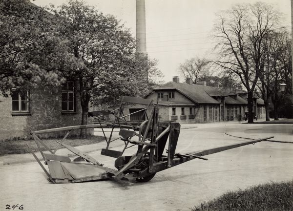 McCormick reaper of 1849 on a road near brick buildings in Copenhagen, Denmark. There is a smokestack in the background.
