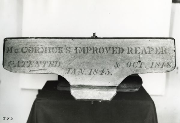 Back of the raker's seat on a McCormick reaper of 1849, showing stenciling that reads: "McCORMICK'S IMPROVED REAPER Patented Jan. 1845, & Oct. 1848". The seat is on a cloth covered display table.