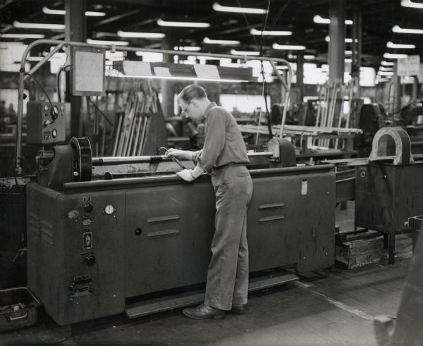 A factory worker operates a Magnaflux machine at International Harvester's 20 millimeter gun plant. Original caption reads: "A Magnaflux machine is used to detect any fissures in each gun tube before it goes too far along the link of operations. The magnetic action of this machine, in which the two sides of a fissure serve as north and south poles, discloses any imperfections."