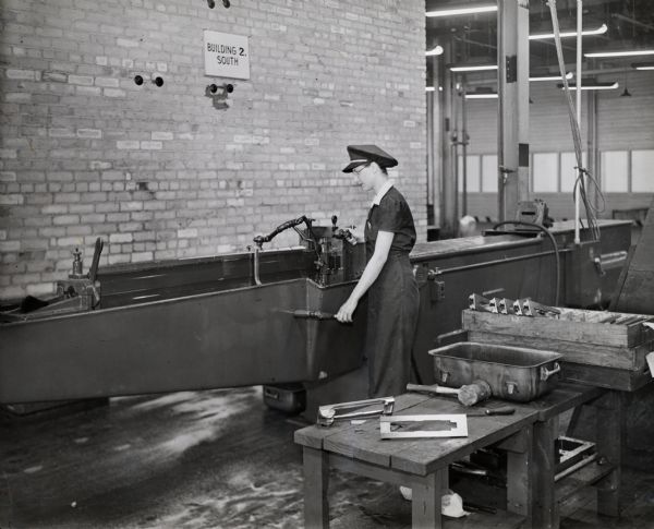 Female factory worker operating a broaching machine at International Harvester's 20 millimeter gun plant. Caption on photograph reads: "This American hydraulic broaching machine is operated by women. It is an H-20/60 horizontal. In their earlier manufacture the Company used milling and filling operations for this job, but have now turned to broaching wherever possible."