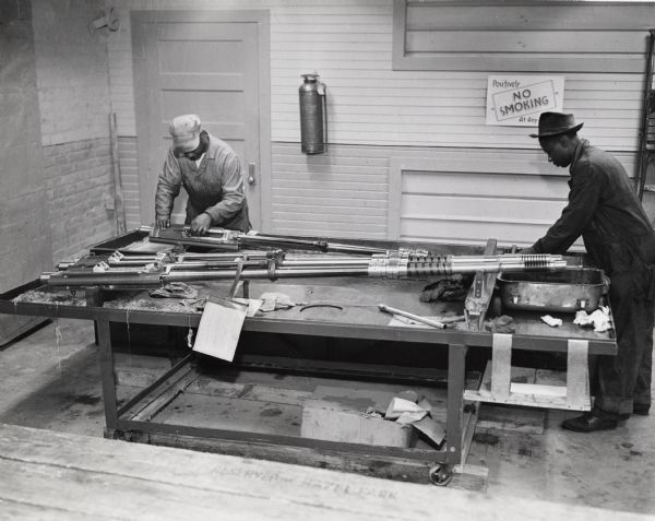 Factory workers inspect a gun at International Harvester's 20 (twenty) millimeter gun plant. Original caption reads: "In the test firing department careful records are kept of the proof firing, function firing and endurance tests on each gun. In addition, the Inspection Department has every gun put through a preliminary cleaning operation after the firing before it goes into the plant for disassembling prior to final assembly and shipment."