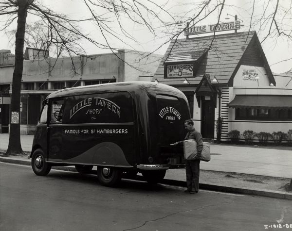 A man holding a package standing next to an International model D-15-M truck with a 113-inch wheelbase and a Metro body. This truck was one of four International trucks owned by Littler Tavern Shops, Inc., a chain of restaurants located in Washington, Baltimore, and Louisville.  According to the original caption, the company operated 45 restaurants in these cities and their suburbs, specializing in five-cent hamburgers. The four Internationals were all used in Washington and Baltimore and they have 41 shops in those two cities. Their trucks average 1200 miles a week.