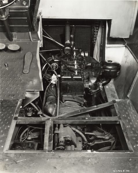 Interior of an International Metro truck with the floorboard removed to show engine and transmission. The pedals and the steering wheel are in the upper left corner.