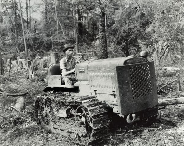 Man using an International T-20 TracTracTor (crawler tractor) in a logging operation. Original caption reads: "F.J. Jacks of Tunica, Mississippi is known all over northern Mississippi as a logger and important retail lumberman. He makes use of seven International power units, four International motor trucks, two International T-20 TracTracTors, and a small McCormick-Deering engine to operate a cement block mixer. Here he is on a T-20, skidding logs in cypress timber."