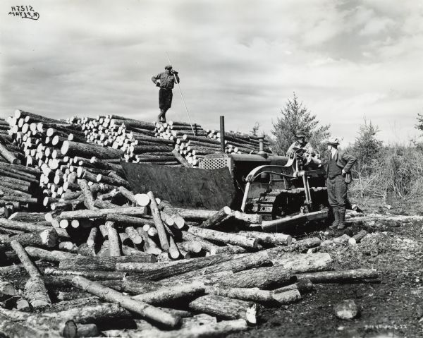 Men with an International TD-35 Diesel TracTracTor (crawler tractor) owned by A.C. Duval. Another man stands on a large pile of logs with a pole in his hand. The men were engaged in logging operations near the Spanish River, west of Sudbury in Ontario, Canada.