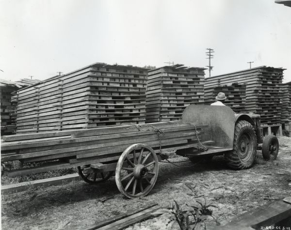 Man pulls a lumber dolly with an International I-12 tractor owned by A.N. Foote Lumber Company. According to the original caption, the dolly was "loaded with 700 board feet, (2,400 ponds) of cypress, which can be hauled at the rate of 10 miles an hour, if desired. Twice as big a load as this can easily be handled by the tractor."