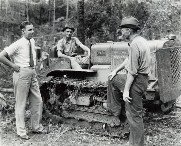 Three men with an International T-20 TracTracTor (crawler tractor). Original caption reads: "F.J. Jacks is known all over northern Mississippi as a logger and important retail lumberman. He makes use of seven International power units, four International motor trucks, two International T-20 TracTracTors, and a small McCormick-Deering engine to operate a cement block mixer. W.W. Rogers of the Memphis branch (left) is talking to E. Robuck, timber foreman (right), and S.S. McCrary, tractor operator (on tractor)."