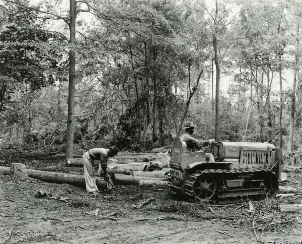 Two men use an International T-20 TracTracTor (crawler tractor) to skid logs in cypress timber. Original caption reads: "F.J. Jacks of Tunica, Mississippi, is known all over Northern Mississippi as a logger and important retail lumberman. He makes use of seven International power units, four International motor trucks, two International T-20 TracTracTors (crawler tractors), and a small McCormick-Deering engine to operate a cement block mixer."