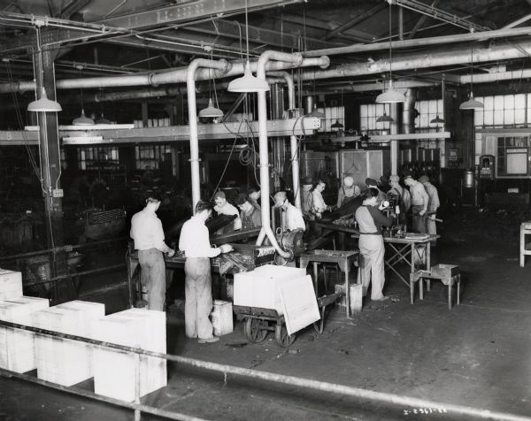 Factory workers inspect shell packing case forgings, possibly at International Harvester's Canton Works. Original caption reads: "This photograph shows the final setting, gauging, Brinnelling, and inspection of shell packing case forgings before the plating operation is performed."