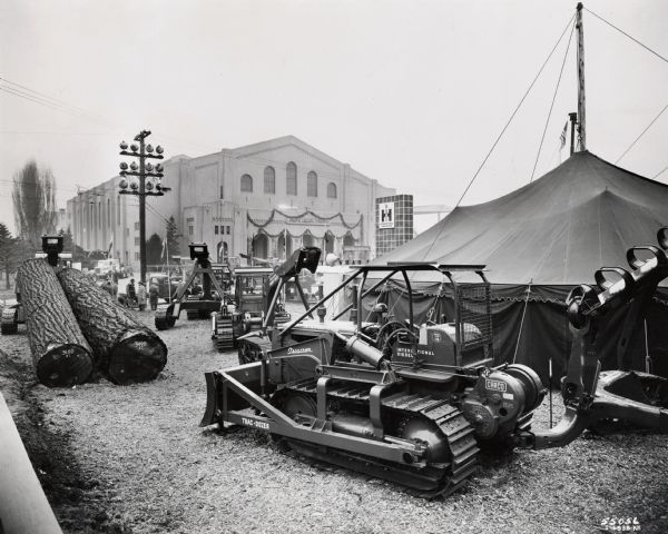 International Harvester equipment, including a TD-18 TracTracTor (crawler tractor), on display at the Pacific Logging Congress. Also on display are two large logs, an International Harvester pylon with logo, and the Pacific Congress building.